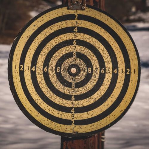 Yellow target for shooting with black circles and numbers on wooden post in countryside with snowy ground on winter day